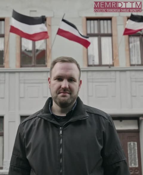 A person standing in front of a building with flagsDescription automatically generated