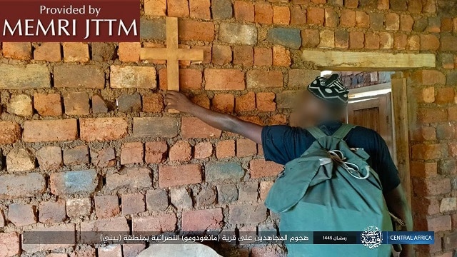 A person with a backpack holding a cross on a brick wallDescription automatically generated